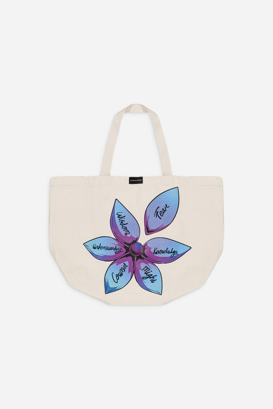 Le sac Flower de WΩRSHIPPER BRAND est un cabas crème à deux anses, orné d'une grande fleur bleue et violette à cinq pétales. Chaque pétale est orné des mots manuscrits suivants : Confiance, Connaissance, Esprit, Courage et Compréhension.
